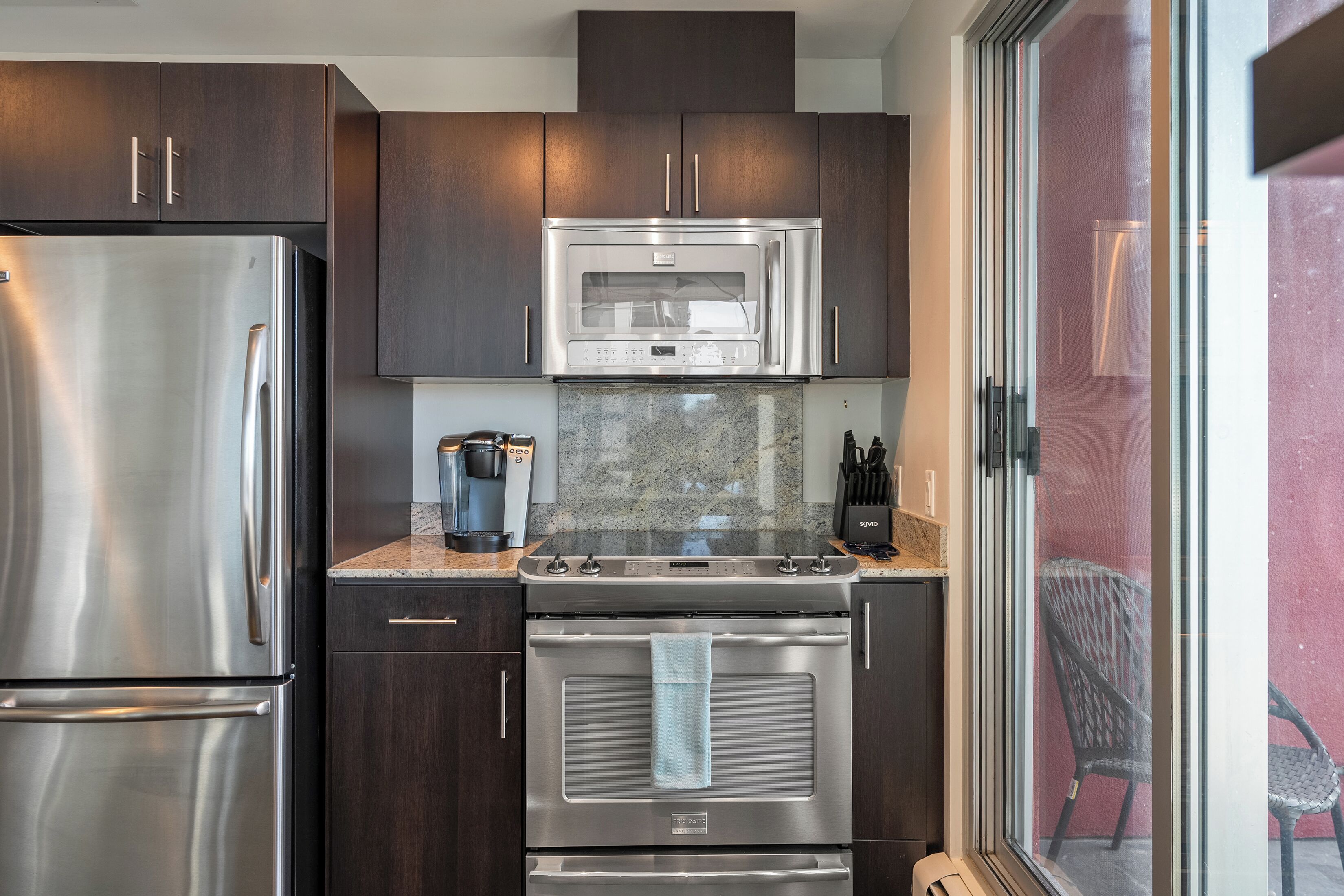 A modern kitchen with stainless steel appliances, dark wood cabinets, and a granite countertop.