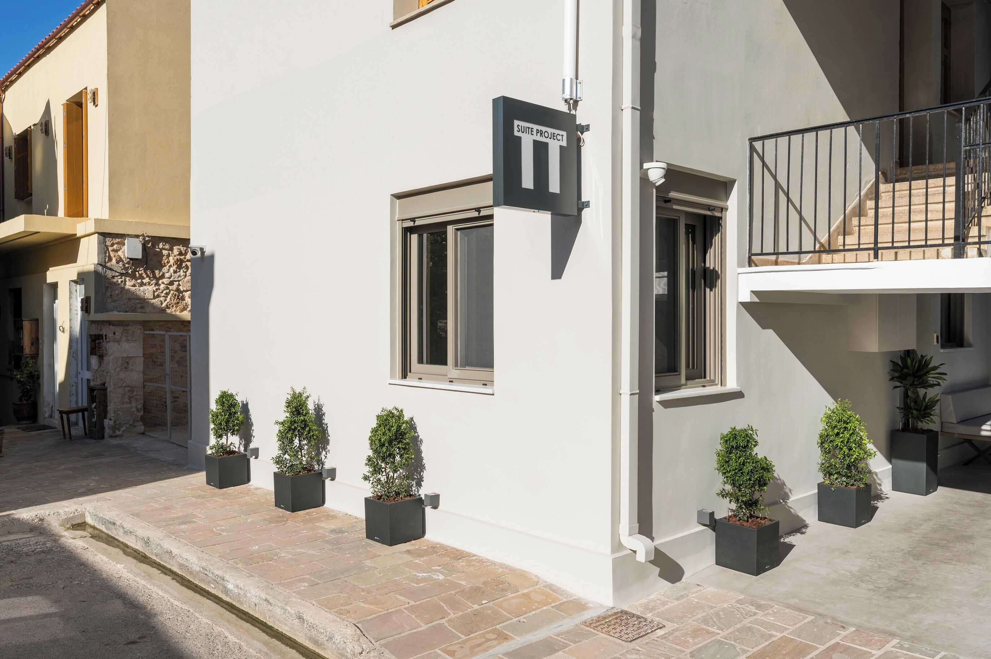 A building with a sign indicating a "Suite Project" and multiple windows. There are potted plants along the exterior wall.