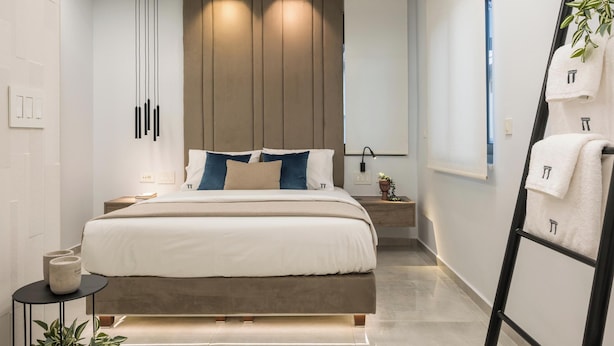 A modern hotel room with a large bed, bedside tables, a wall-mounted TV, and a plant. - Pi Suite Project Smart Living (Chania)