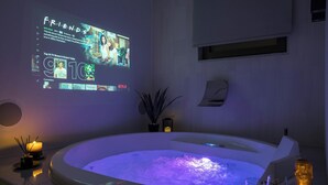 A modern spa area with a heated tub, a projection screen displaying TV shows, and a cozy ambiance with candles and a bottle of champagne. - Pi Suite Project Smart Living (Chania)