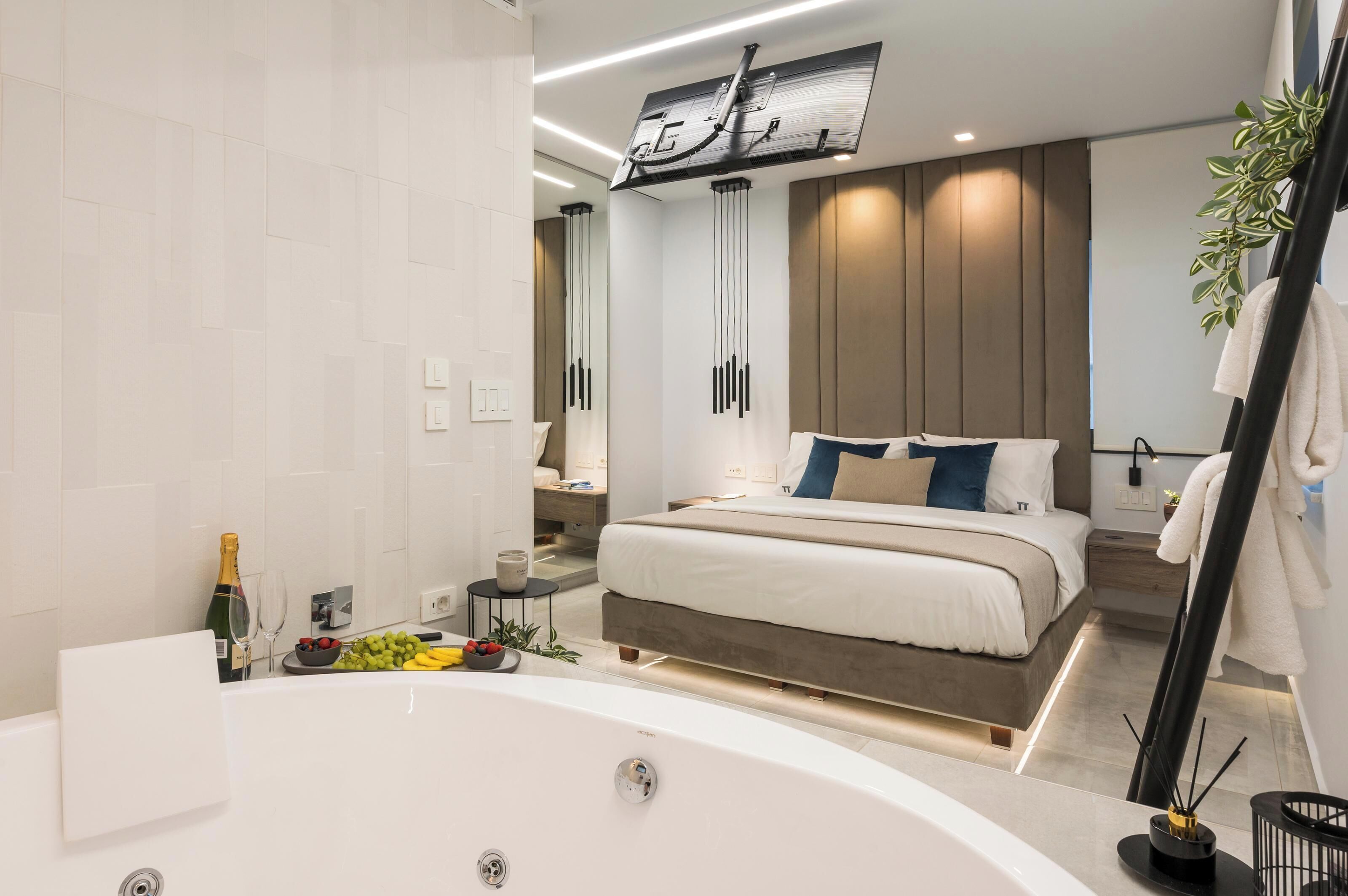 A modern bedroom with a large bed, a bathtub, and a TV mounted on the wall.