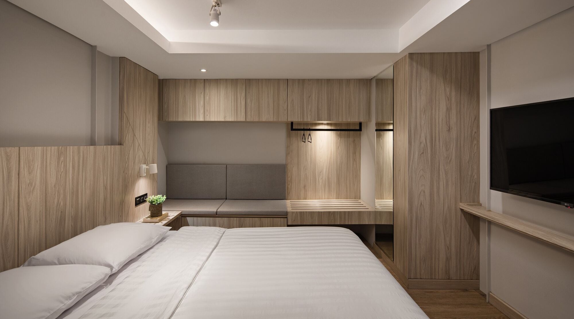 Une chambre moderne dotée d’un grand lit, d’un coin salon intégré et d’un téléviseur fixé au mur.