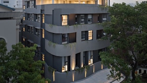 Ein mehrgeschossiges Gebäude mit einer geschwungenen Dachterrasse, mehreren mit Pflanzen bepflanzten Balkonen und einem modernen architektonischen Design.