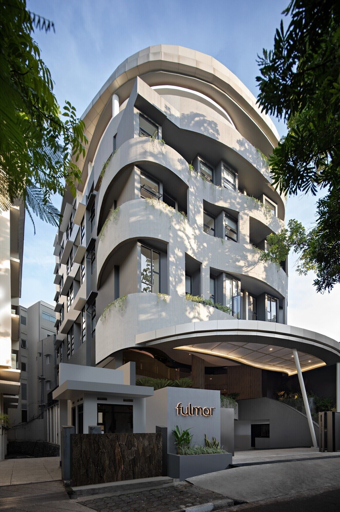 Un edificio moderno con fachada curva, varios balcones y una zona de entrada cubierta.
