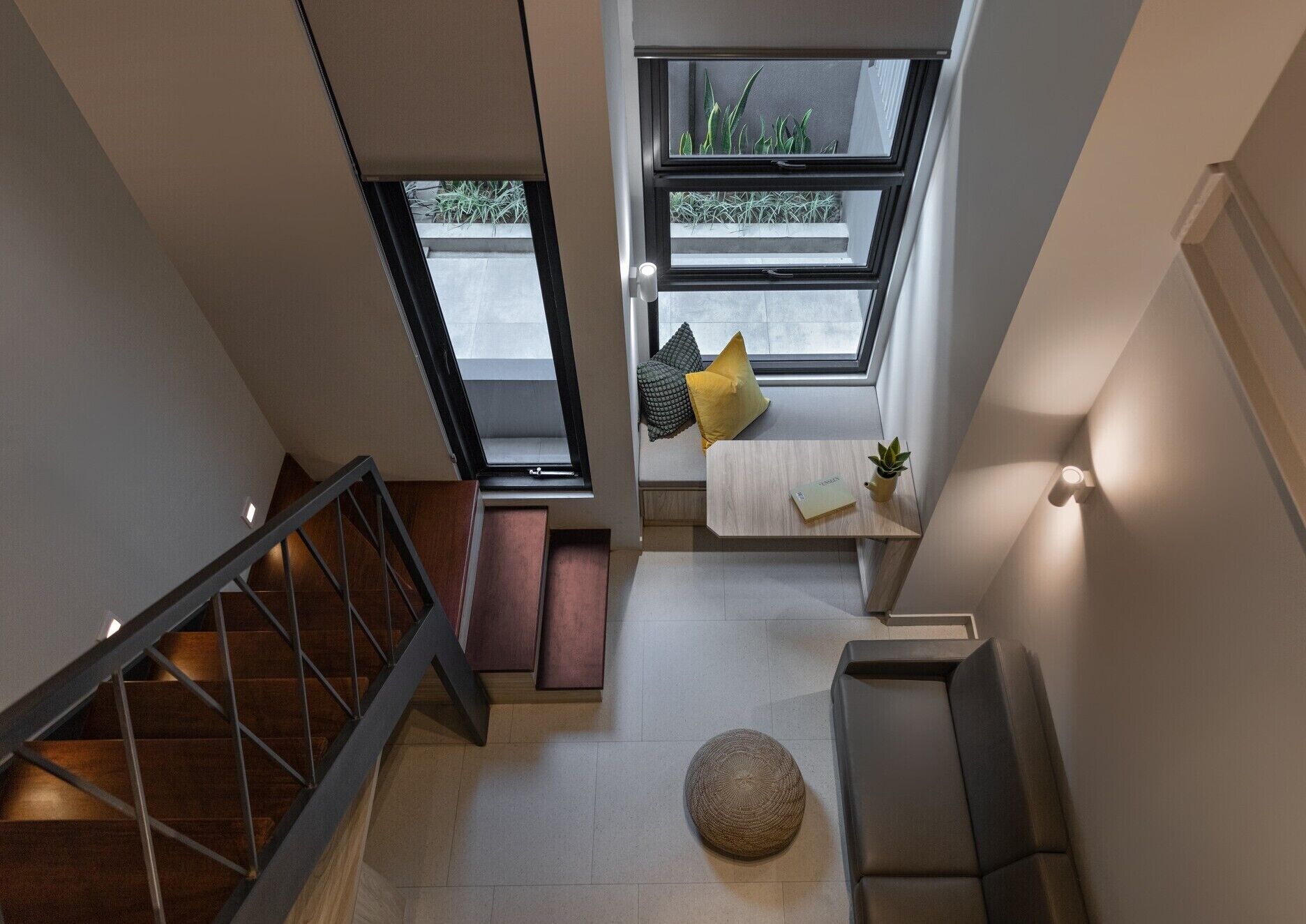 Ein modernes Interieur mit einer Treppe, einer Sitzecke mit Kissen, einem kleinen Tisch und einem Topfpflanzen.