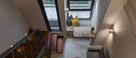 A modern interior with a staircase, a seating area with cushions, a small table, and a potted plant.