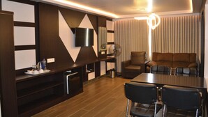 A modern hotel room with a dining area, a sofa set, a TV mounted on the wall, and a fan. - Hotel Free Birds  (Tiruchirappalli)