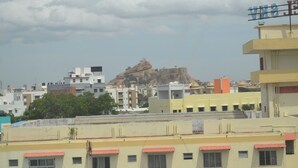 A cityscape with a prominent hill in the background, surrounded by buildings with flat roofs and some greenery. - Hotel Free Birds  (Tiruchirappalli)
