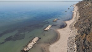 Luchtbeeld van een kustgebied met een zandstrand, rotsformaties en een helder uitzicht op de zee.