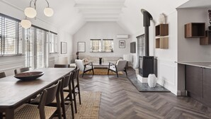 Een ruime woonkamer met een eettafel, stoelen, een open haard en grote ramen.