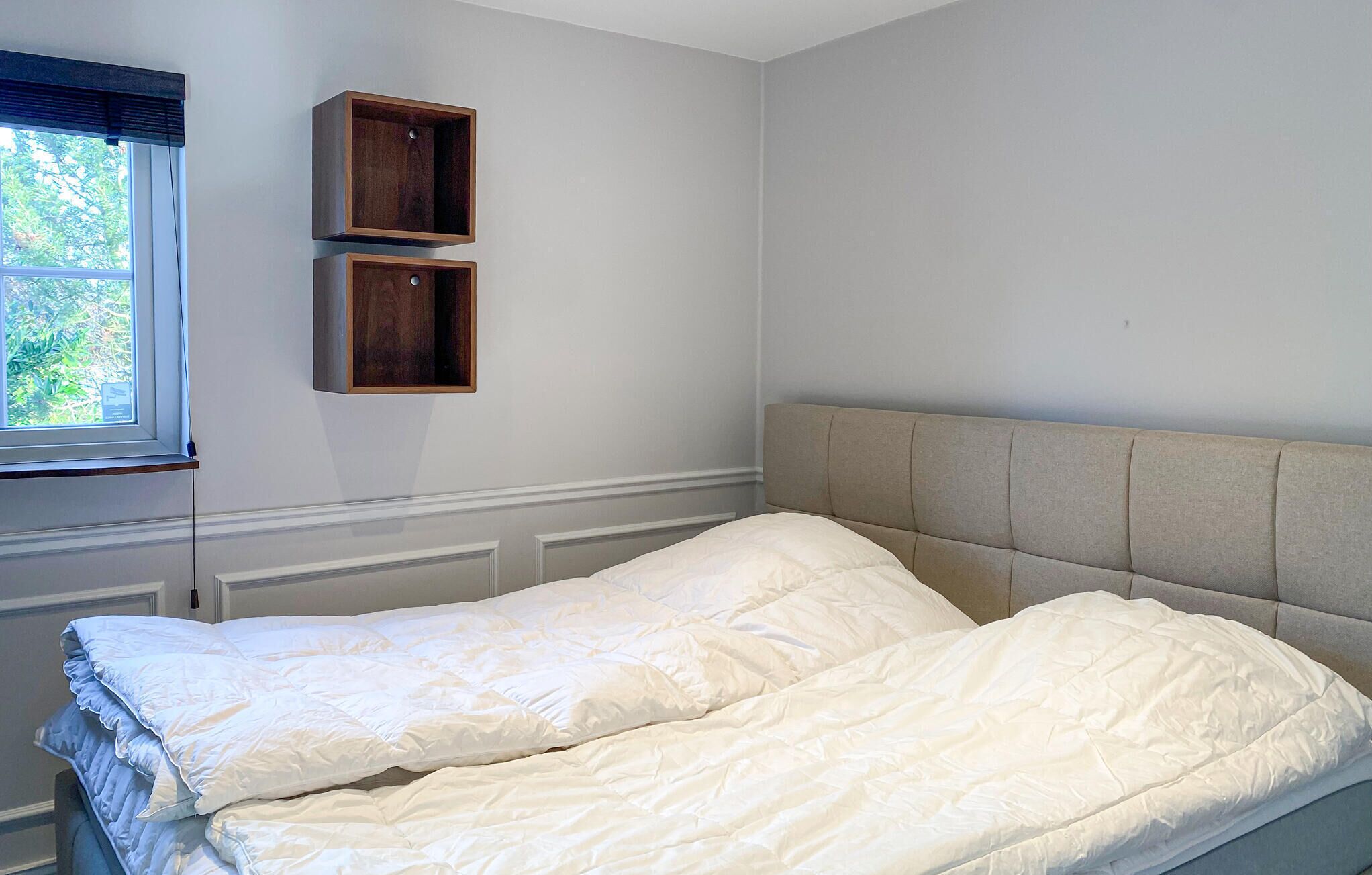 A bedroom with a bed, two wooden shelves, a window, and a radiator.