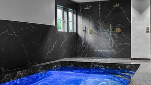 Een moderne badkamer met een wand van zwart marmer, een blauw tintje hebbend bad en een raam met uitzicht op groen.