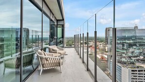 A balcony with glass railings, a sofa, and a chair, offering a city view. - High-rise Apt Raleigh Free Parking Sunset View 1 (Raleigh)