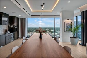 A modern conference room with a long wooden table, large windows offering a city view, and a potted plant. - High-rise Apt Raleigh Free Parking Sunset View 1 (Raleigh)