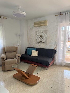 A living room with a sofa, armchair, and a glass coffee table.