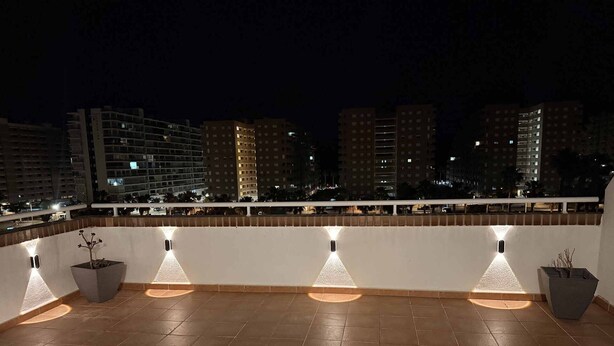 Une terrasse sur le toit, dotée d’un sol carrelé, de plantes en pot et de luminaires fixés aux murs.