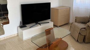 Un salon avec un téléviseur à écran plat, une table basse en verre, un canapé beige et un meuble en bois.