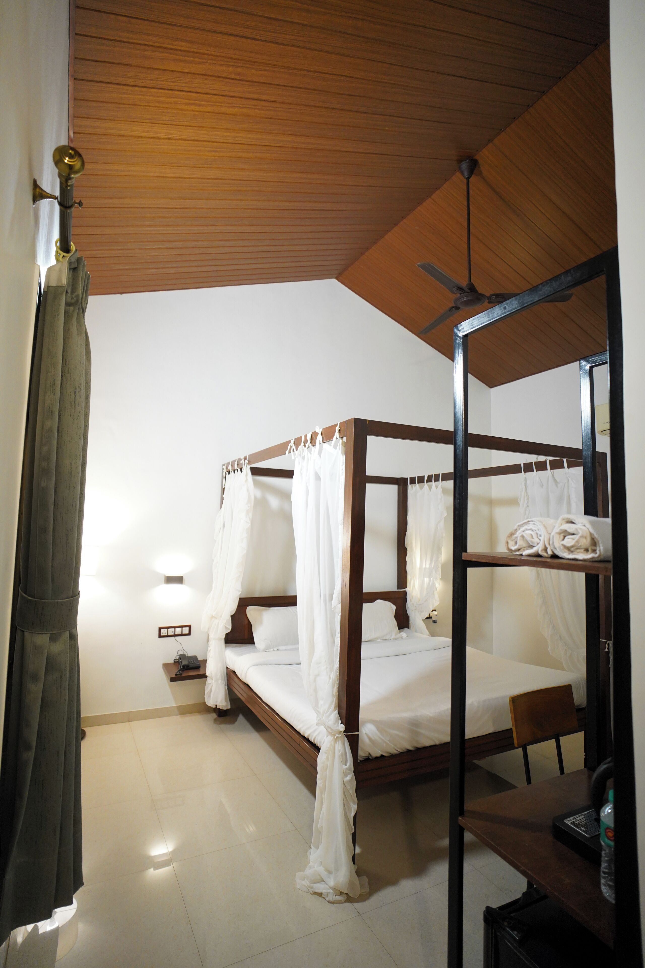 A bedroom with a wooden ceiling, a bed with white bedding, a bedside table, and a chair.