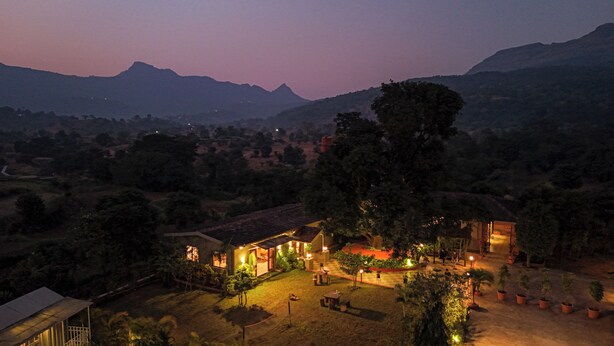 A hotel with a well-lit courtyard, surrounded by lush greenery and mountains in the background. - Vanah Villa And Resort (Mawal)