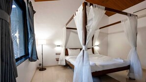 A four-poster bed with white canopies, a bedside lamp, and a view of the outdoors through a window with curtains. - Vanah Villa And Resort (Mawal)