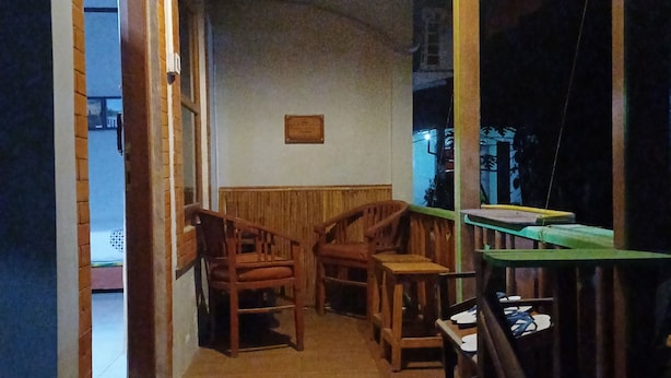 Une terrasse en bois avec un banc et une table, une porte donnant sur l’extérieur et un luminaire fixé au mur.