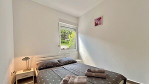 A bedroom with a bed, a nightstand, a lamp, and a window with a view of greenery. - Apartman Velly  (Jadranovo)