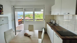 A modern kitchen with white cabinets, a wooden countertop, and a view of a green landscape through large windows. - Apartman Velly  (Jadranovo)