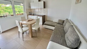 A modern kitchen with white cabinets, a dining table with chairs, and a gray sofa. - Apartman Velly  (Jadranovo)