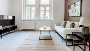 Ein modernes Wohnzimmer mit einer Couch, einem Couchtisch, einem Fernseher und einem großen Fenster mit Blick auf Gebäude.