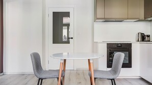 Eine moderne Küche mit einem weißen Tisch und zwei grauen Stühlen, einer Tür mit Milchglasfenster und einem Edelstahlbackofen.