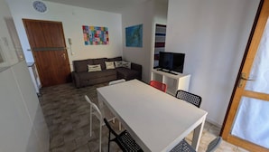 A compact living space with a kitchenette, a sofa, a dining table, and a TV. - Welcoming Flat With a Magnificent Terrace (San Michele al Tagliamento)