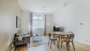 A modern living room with a sofa, coffee table, and dining table with chairs. There is a TV and a window with curtains. - Blueground | Prague 3, close to offices & mall (PRG-20) (Prague)