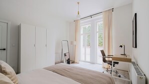 Et moderne hotelværelse med en stor seng, et skrivebord med stol, et spejl og et vindue med gardiner.