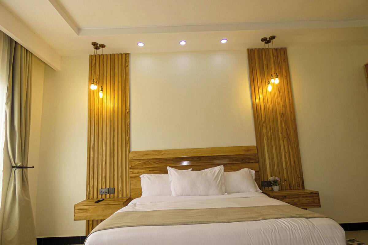 Una habitació d'hotel amb un llit gran, un capçal de llit de fusta i dues taules de nit amb làmpades.