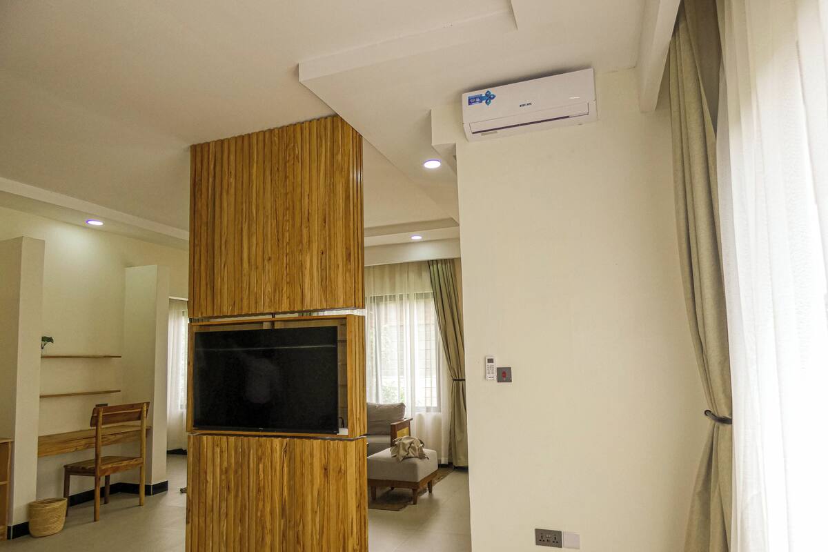 Habitació d'hotel moderna amb un moble d'entreteniment de fusta, televisió de pantalla plana, sofà i zona de menjador.