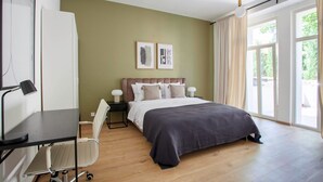 A modern bedroom with a bed, desk, chair, and large windows.
