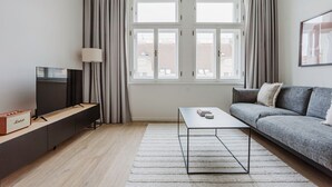 Un soggiorno moderno con una TV a schermo piatto, un divano, un tavolino da caffè e una finestra con tende.
