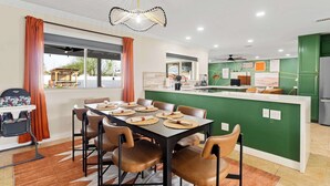 A modern kitchen with green cabinets, a dining area with a table set for four, and a baby changing station. - The Ridge: Family | Pickleball | Pool | Hot Tub (Phoenix)