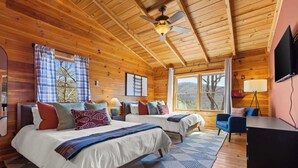 Une chambre dans un chalet en bois, avec deux lits, un ventilateur de plafond, un bureau et une télévision.