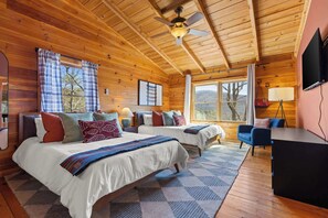 Ein Schlafzimmer einer Holzhütte mit zwei Betten, einem Deckenventilator, einem Schreibtisch und einem Fernseher.