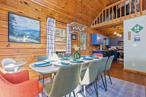 Ein Holzblockhaus-Innenraum mit einem Esstisch für sechs Personen, einer Küche mit blauen Schränken und einem großen Gemälde an der Wand.