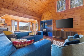 Ein Innenraum einer Blockhütte mit einem großen Fernseher, blauen Sofas und einem Kamin aus Stein.