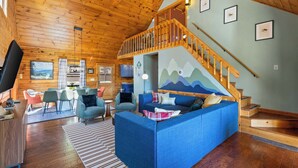 Un intérieur en bois avec un canapé, des fauteuils, un téléviseur et un escalier.