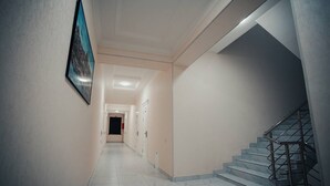 A hallway with a staircase, white walls, and a framed picture on the wall. - Bagishamol Hotel (Urgut)