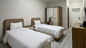 A hotel room with two beds, a desk, and a wardrobe. - Bagishamol Hotel (Urgut)