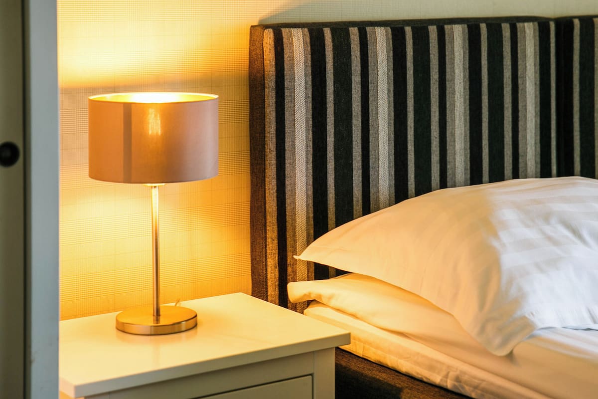 A neatly made bed with white linens, a striped headboard, and a bedside lamp on a white nightstand.