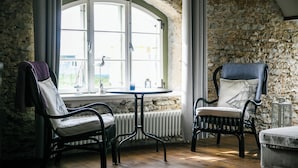 Una habitación acogedora con pared de piedra, una mesa redonda, dos sillas y vistas amplias por un gran ventanal.