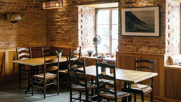 Un comedor rústico con vigas de madera a la vista, paredes de ladrillo y mesas y sillas de madera.