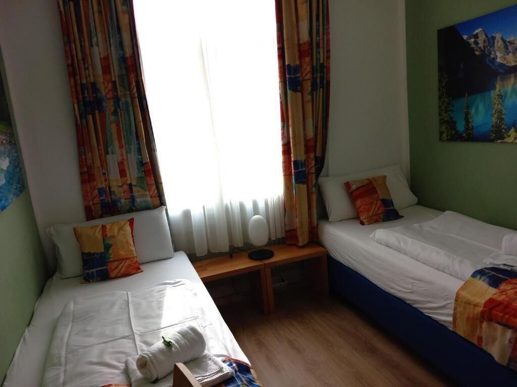 A room with two beds, a window with curtains, a radiator, and a painting on the wall.