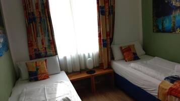 A room with two beds, a window with curtains, a radiator, and a painting on the wall.